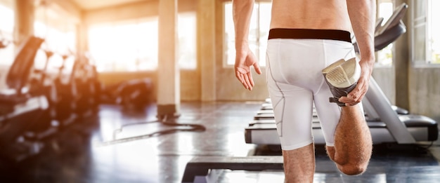 Healthy lifestyle and Relaxation. Behind muscular handsome man stretching leg warming before workout in gym fitness.