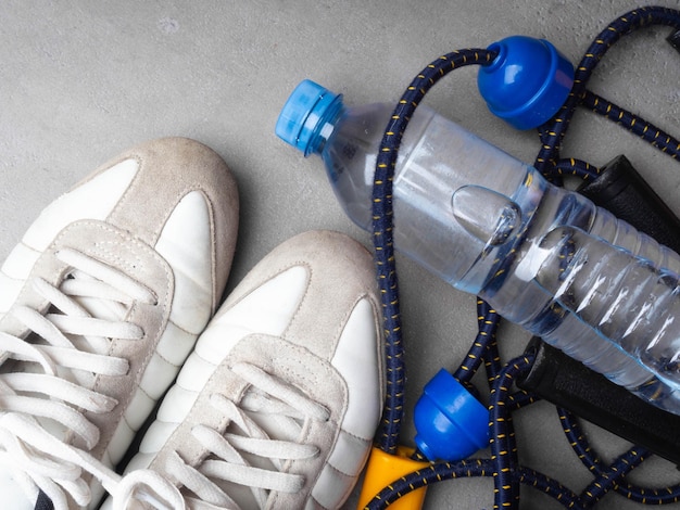 Healthy lifestyle and sport concept White sneakers expander and bottle of water on a grey background