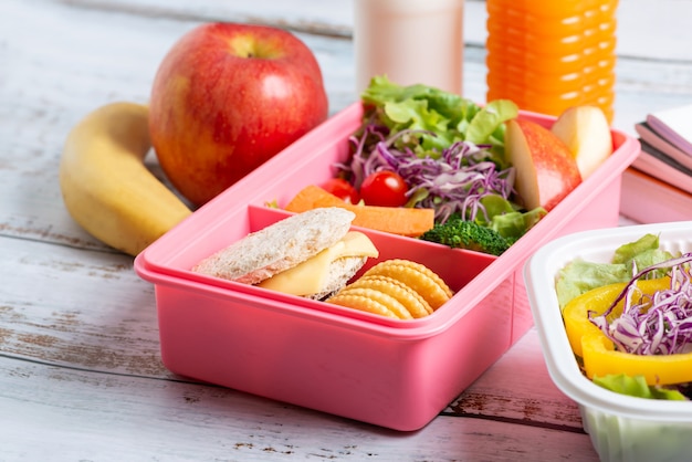 Healthy lunch box set of sandwich cheese with cracker and salad in box, banana and apple, orange juice and milk.