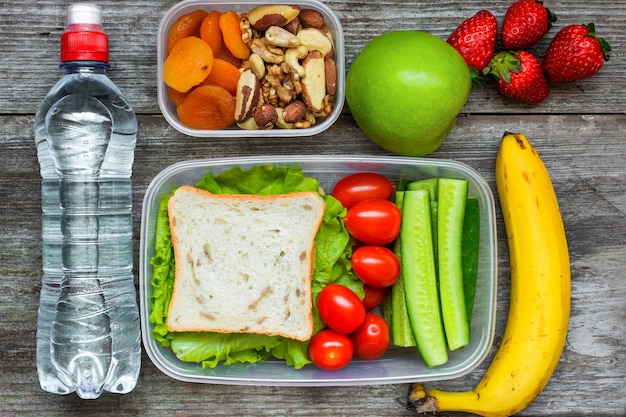 Healthy lunch boxes with sandwich and fresh vegetables, bottle of water, nuts and fruits