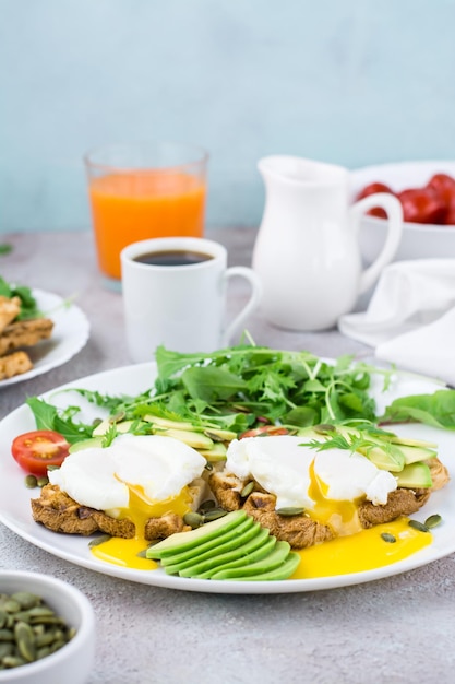 Healthy lunch. Toast with poached eggs, avocado pieces, arugula, mizuna and chard leaves and cherry tomatoes on a plate on a served table. Flexetarian diet. Vertical view