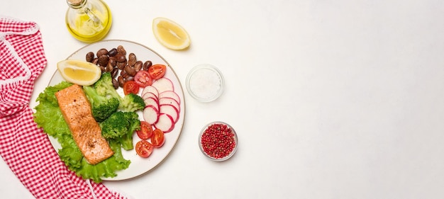 Healthy lunch with grilled salmon on green lettuce next to vegetables tomatoes radishes broccoli