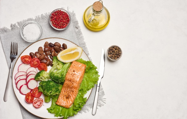 Healthy lunch with grilled salmon on green lettuce next to vegetables tomatoes radishes broccoli