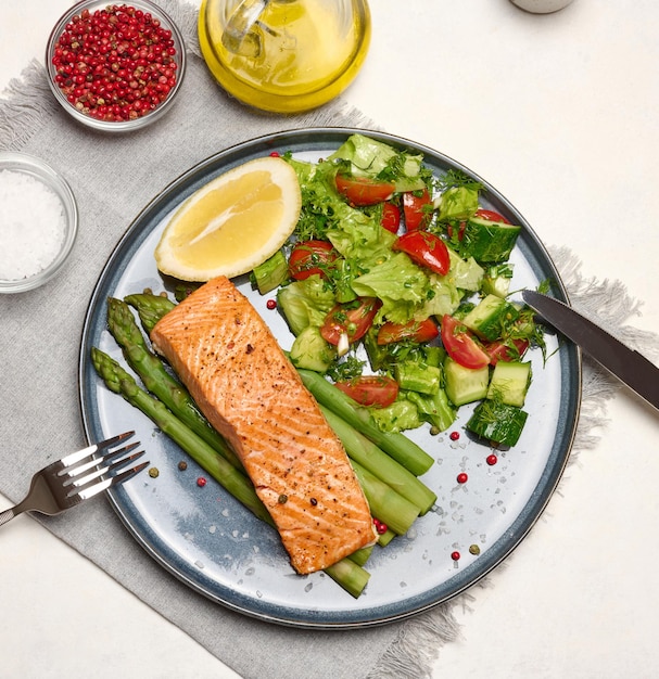 Healthy lunch with grilled trout with asparagus and fresh tomato and cucumber salad a lemon slice