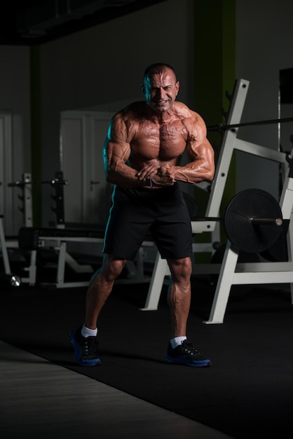 Healthy Mature Man Standing Strong In The Gym And Flexing Muscles  Muscular Athletic Bodybuilder Fitness Male Posing After Exercises