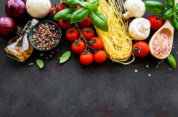 Healthy mediterranean diet with spaghetti, tomatoes, basil, olive oil, garlic, peppers on black surface