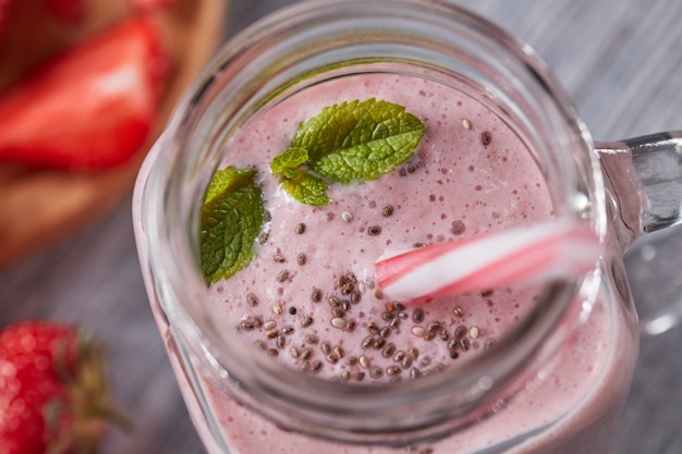 Healthy milk drink with strawberries, chia seeds and fresh mint in a jar with a straw