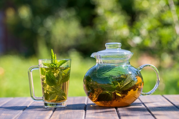 Photo healthy nettle tea in a glass tea pot and mug in the summer garden on wooden table