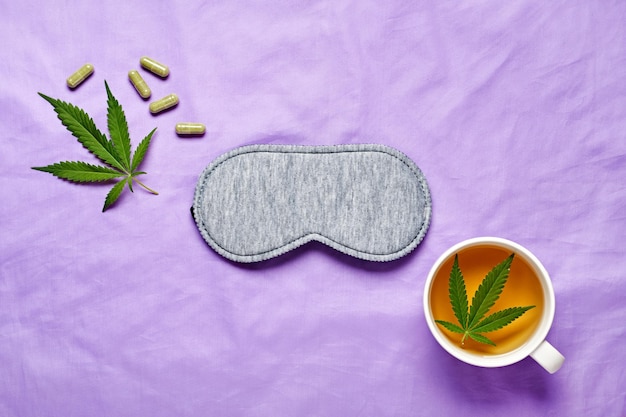 Healthy night sleep concept Sleep mask calming hemp tea and hemp capsules on silk lilac background