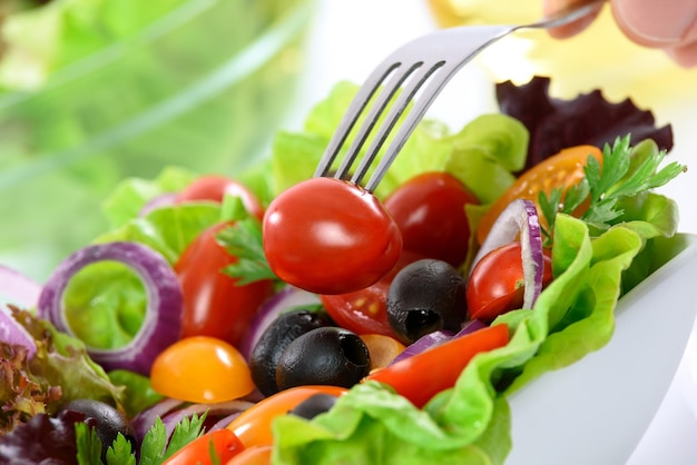 Healthy nutrition mixed vegetable salad in a bowl on the table and a hand holding a fork with tomato