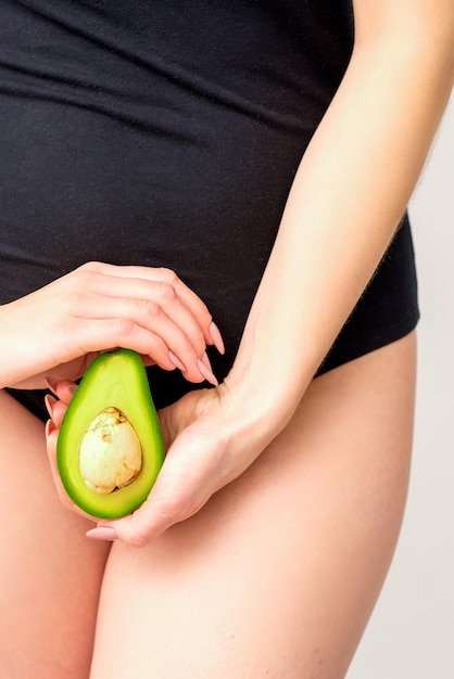 Healthy nutrition and pregnancy concept Young woman holding one half of an avocado fruit close to her belly over a white background