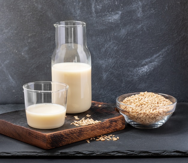 Healthy oat milk in glass bottle and glass and oat seeds on glass bowl