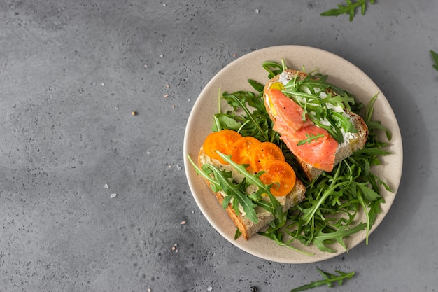 Healthy open sandwiches with artisan bread with cream cheese, salmon, tomatoes and arugula