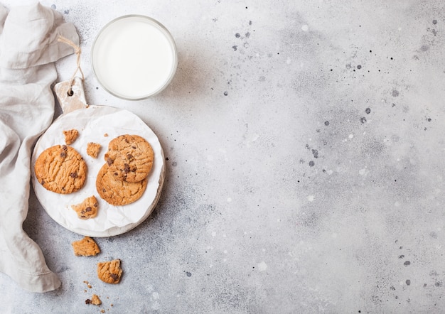 Healthy organic oat cookies with chocolate with glass of milk on wooden board on stone kitchen table.