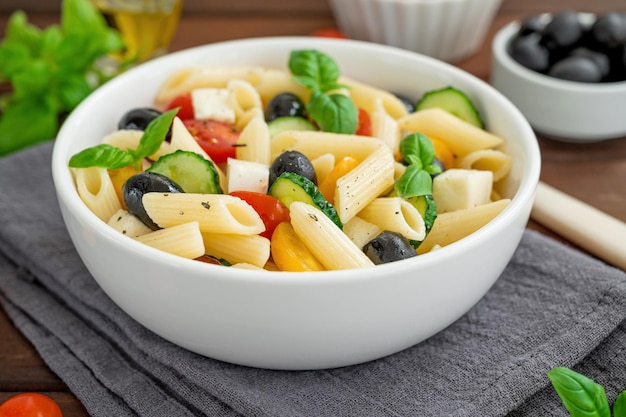 Healthy pasta salad with tomatoes cucumbers red onions olives and cheese in a bowl Copy space