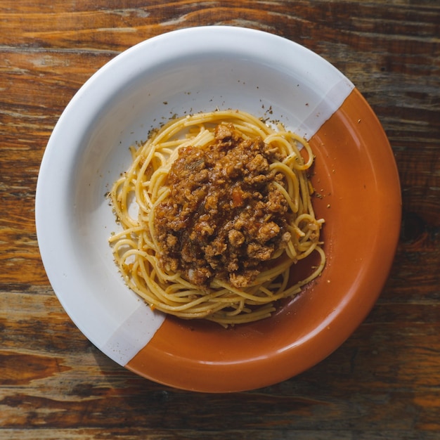 Healthy plate of Italian spaghetti topped with a tasty tomato and ground beef Bolognese sauce and fresh basil on a rustic brown wooden table