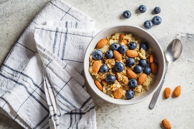 Healthy quinoa porridge with blueberries and almonds with syrup in gray bowl, copy space. Vegan food concept.