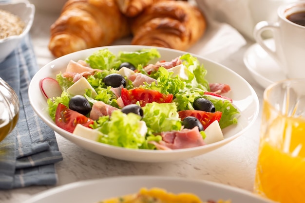 Healthy salad in a bowl with olives raddishes tomato cheese and lean ham served for breakfast