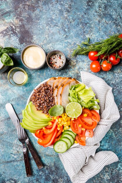 Healthy salad bowl with quinoa, tomato turkey, avocado, sweet pepper, corn, lime and mixed greens, top view. Healthy food conception. Superfood meal.