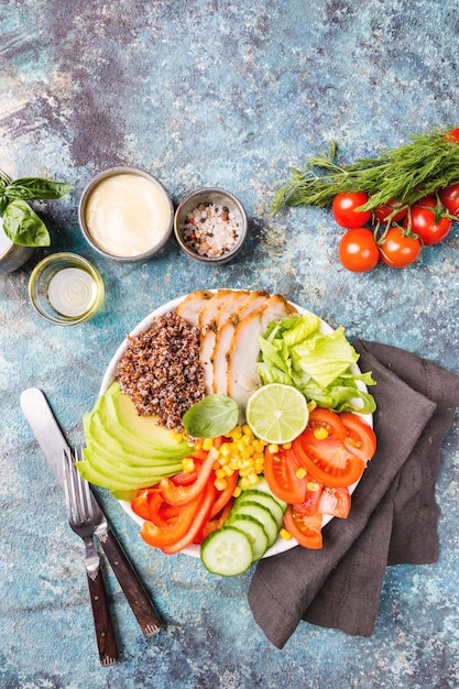 Healthy salad bowl with quinoa, tomato turkey, avocado, sweet pepper, corn, lime and mixed greens, top view. Healthy food conception. Superfood meal.