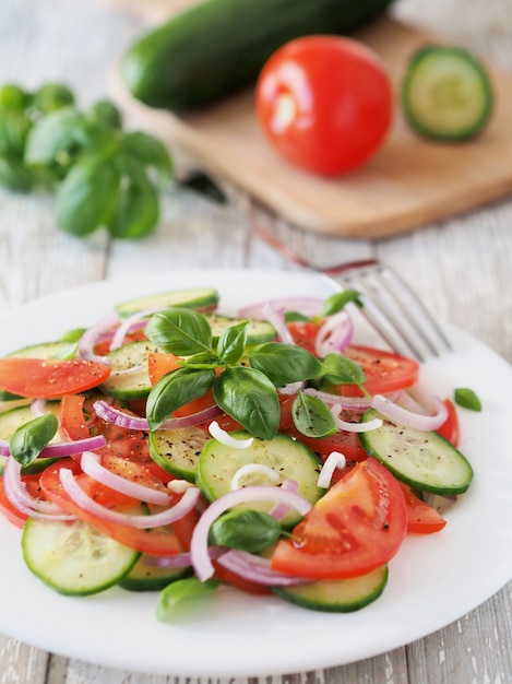 Healthy salad of fresh tomatoes and cucumbers with basil on a white rustic table