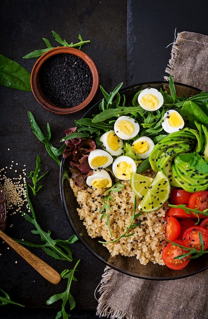 Healthy salad of fresh vegetables - tomatoes, avocado, arugula, egg, spinach and quinoa on bowl. Flat lay. Top view.