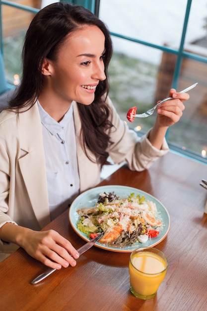 Healthy salad. Top view of appealing attractive sincere woman using fork while smiling and eating salad