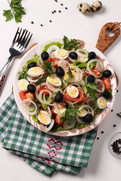 Healthy salad with canned tuna, tomatoes, quail eggs, black olives, white onions and organic lettuce on wooden board on white surface, Vertical format