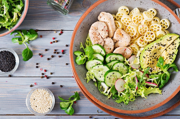 Photo healthy salad with chicken, avocado, cucumber, lettuce, radish  and pasta on dark