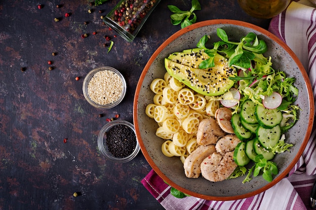 Healthy salad with chicken, avocado, cucumber, lettuce, radish  and pasta on dark