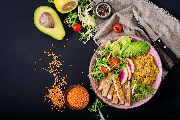 Healthy salad with chicken, tomatoes, avocado, lettuce, watermelon radish and lentil on dark table.