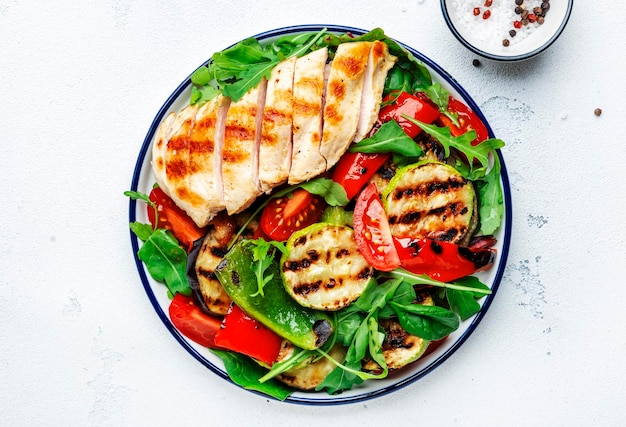 Healthy salad with grilled chicken breast fillet and vegetables paprika zucchini eggplant fresh tomatoes and mixed herbs White table background top view