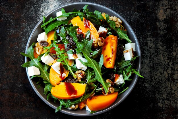 Healthy salad with persimmon, arugula, nuts and feta cheese.