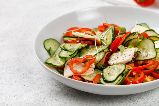 Healthy salad with sliced cucumbers feta cheese sweet peppers in a white plate Fresh green snack