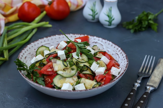 Healthy salad with zucchini, tomatoes and feta, dressed with olive oil in a plate on a dark surface, horizontal orientation