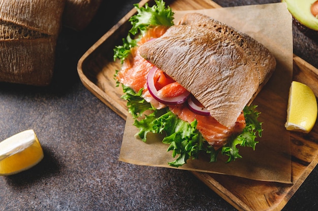 Healthy sandwich with rye bread bun salmon avocado onion and salad served on a wooden rustic board