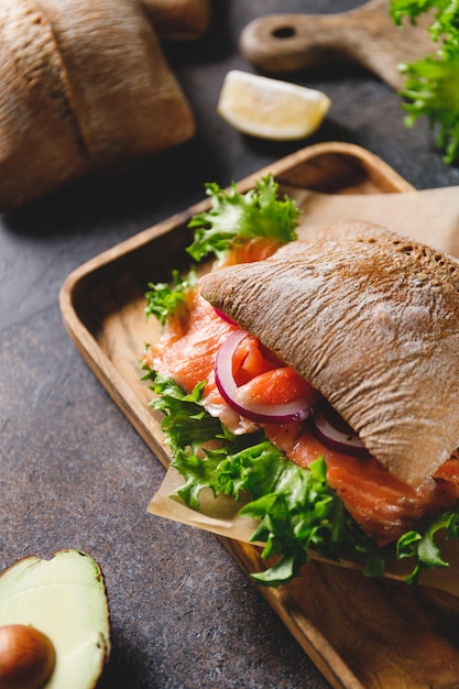 Healthy sandwich with rye bread bun salmon avocado onion and salad served on a wooden rustic board