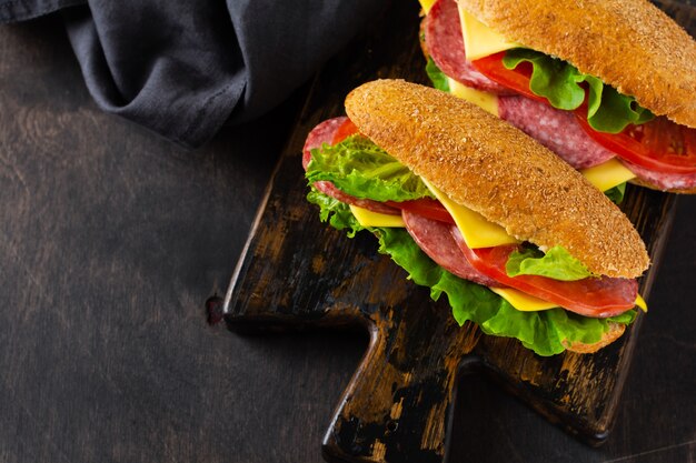 Healthy sandwiches with bran bread, cheese, green lettuce, tomato and sliced salami on rustic wooden stand. Breakfast concept. Top view