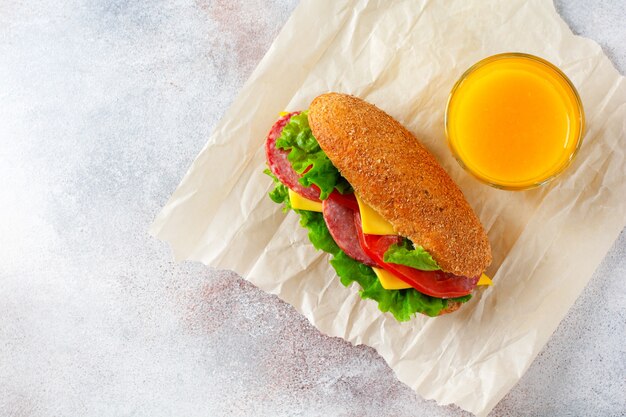 Healthy sandwiches with bran bread, green lettuce, cheese, red tomato and sliced salami on parchment paper and rustic wooden stand. Breakfast concept. Top view