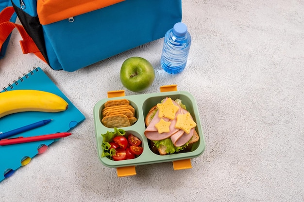 Healthy school lunch box with sandwich and salad on the workplace near backpack School supplies books apple and a bottle of water