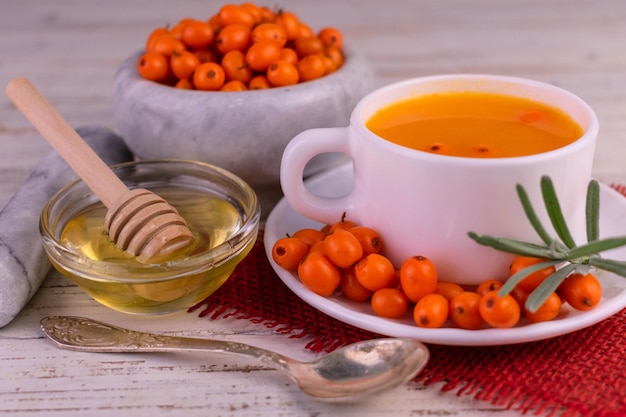 Healthy sea buckthorn and honey tea on a white wooden background.