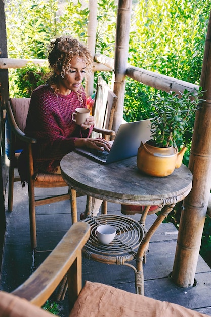 Photo healthy serene woman sitting outdoor at home in patio with green nature background and using laptop with wireless connection concept of alternative office and job surfing the net leisure person