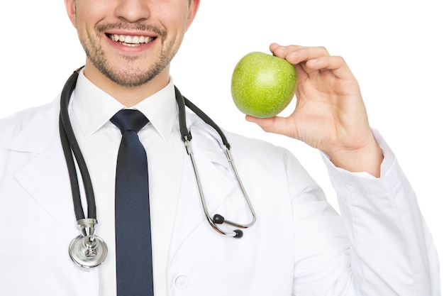 Healthy smile. Cropped closeup shot of a male doctor smiling happily holding an apple isolated on white