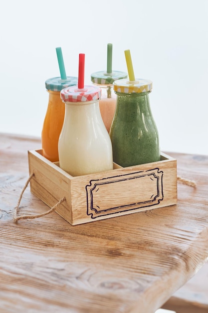 Healthy smoothies served in glass bottles with colorful straws in box on wooden table