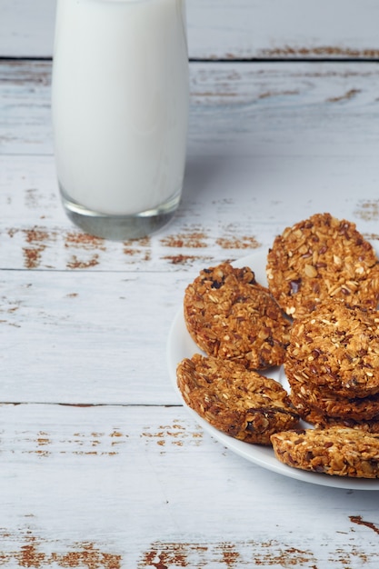 Healthy snack granola whole grain cookies and glass cup of milk on wooden surface.