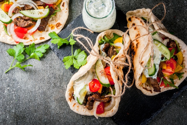 Photo healthy snack, lunch. traditional greek wrapped sandwich gyros - tortillas, bread pita with a filling of vegetables, beef meat and sauce tzatziki