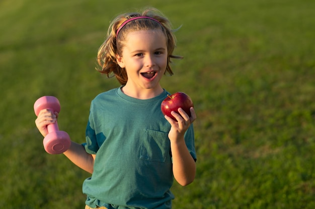 Healthy sporty child with apple and dumbbell outdoor in park Cute little boy doing exercises with dumbbells Portrait of sporty child with dumbbells Happy child boy exercising