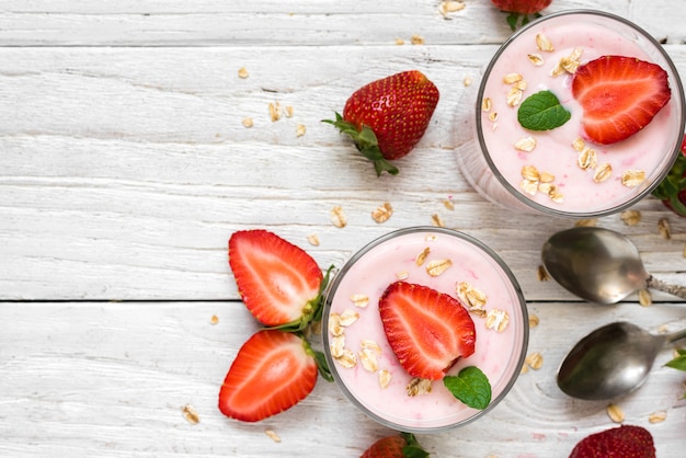 Healthy strawberry yogurt with oats and mint in glasses with fresh berries and spoons over white wooden table