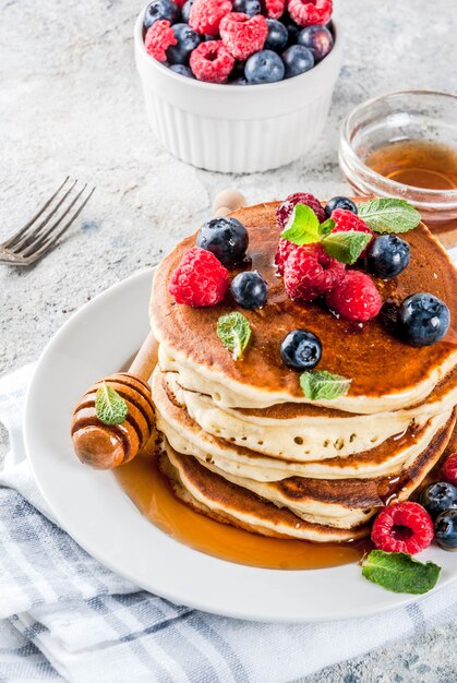 Healthy summer breakfast,homemade classic american pancakes with fresh berry and honey, morning light grey stone surface 