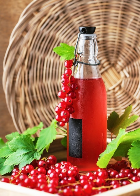 Healthy summer non alcoholic drink of red currant syrup in a glass bottle on a wooden tray